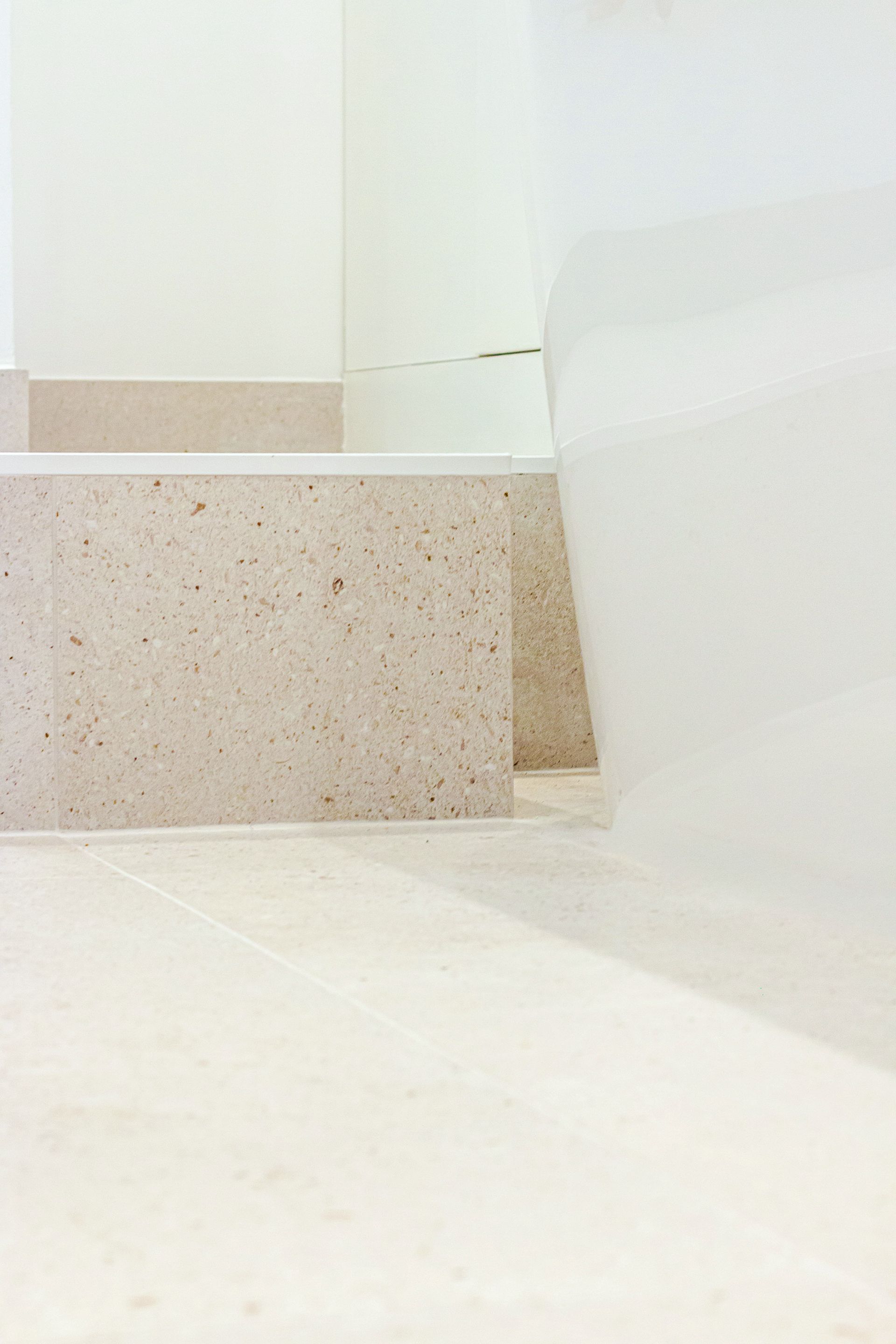 Angle d'une salle de bains beige et blanche avec plateforme surélevée et baignoire courbée.