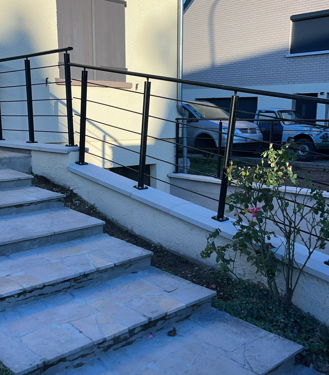 Rampe en métal noir sur des marches en pierre menant à un bâtiment avec un mur beige.