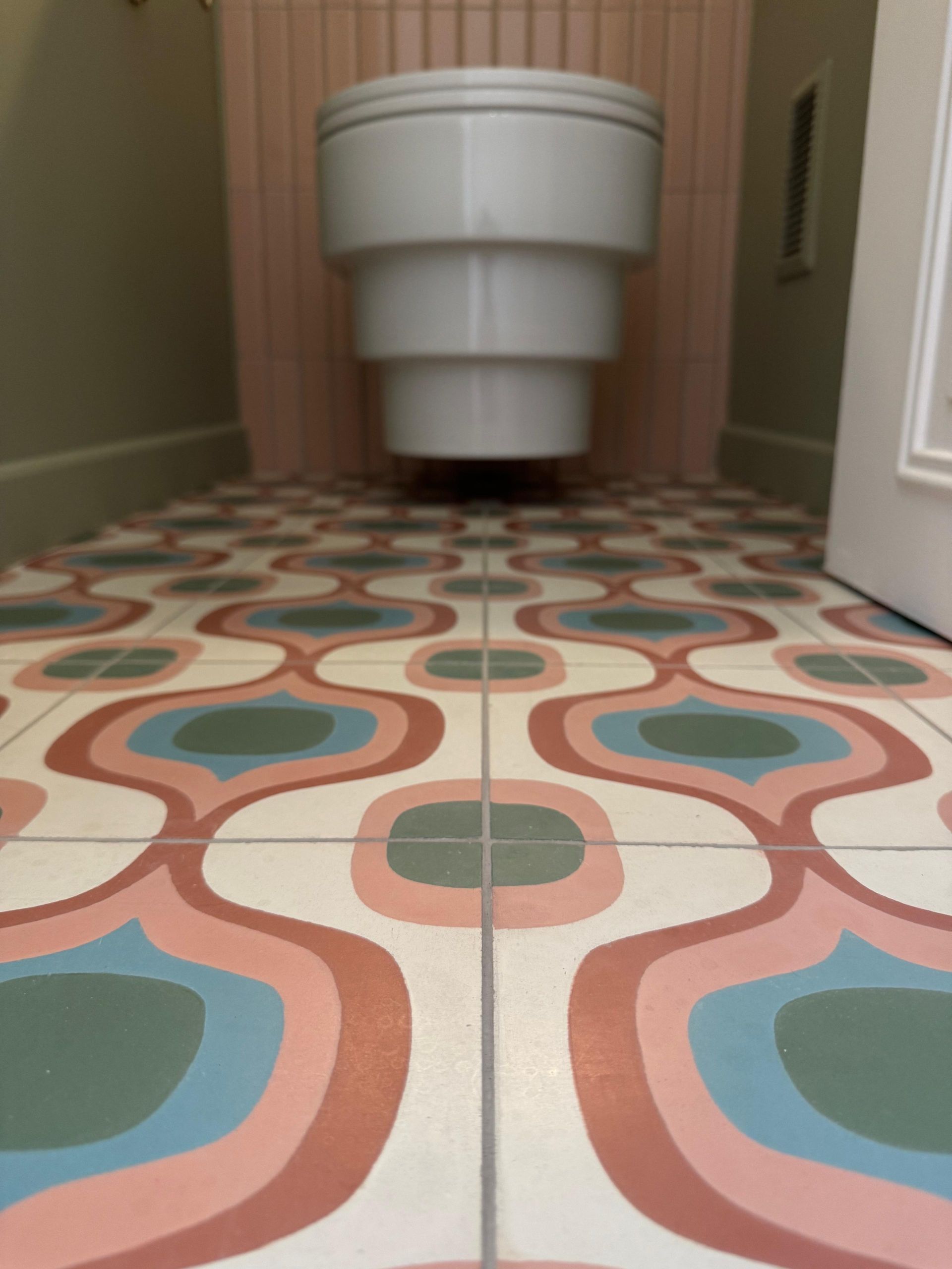 Porte-papier toilette chromé monté sur un mur en carrelage géométrique texturé de couleur pêche.