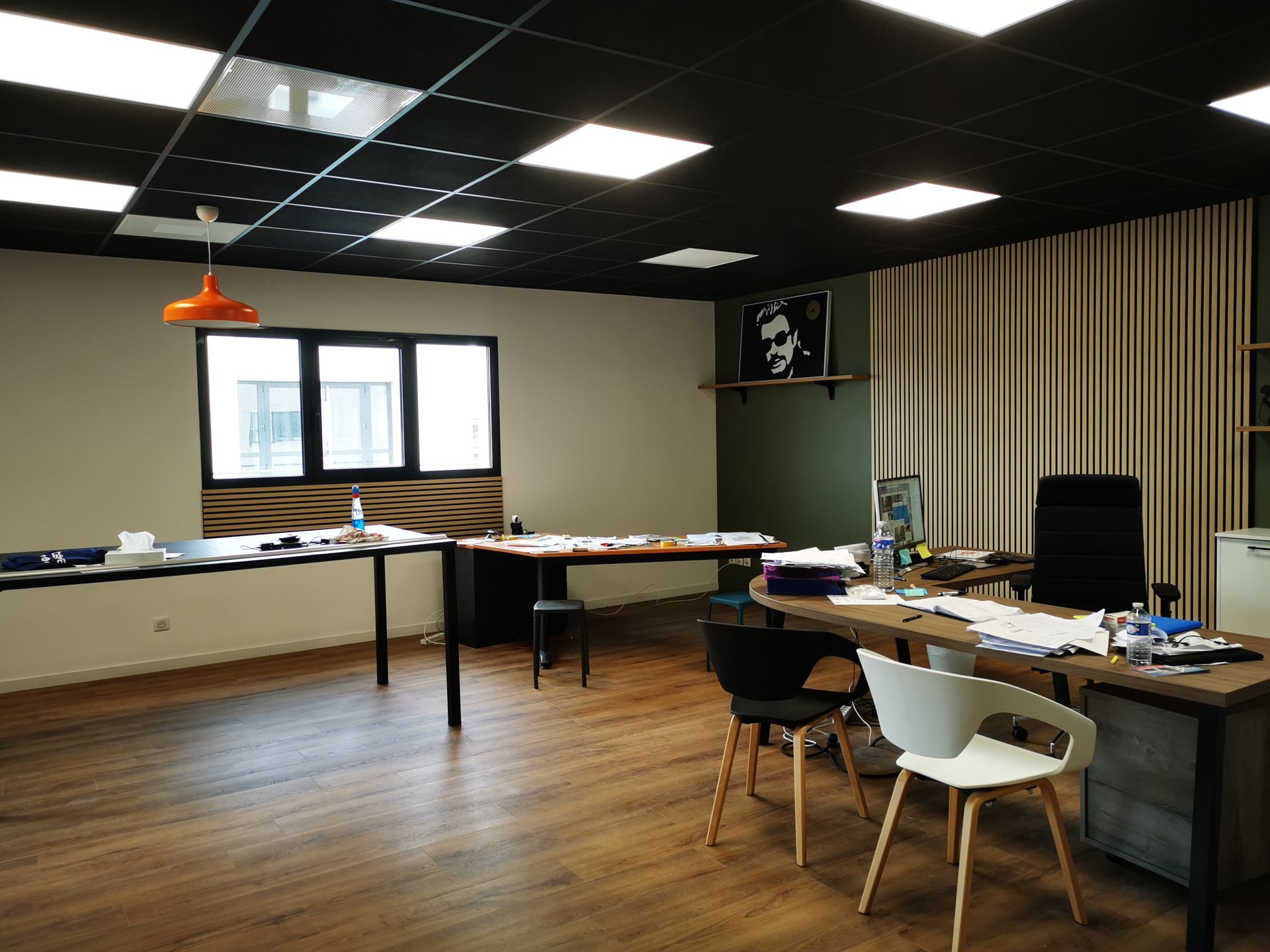 Un espace de bureau moderne avec un plafond noir, un parquet, deux grands bureaux, des chaises et de grandes fenêtres avec des rideaux.