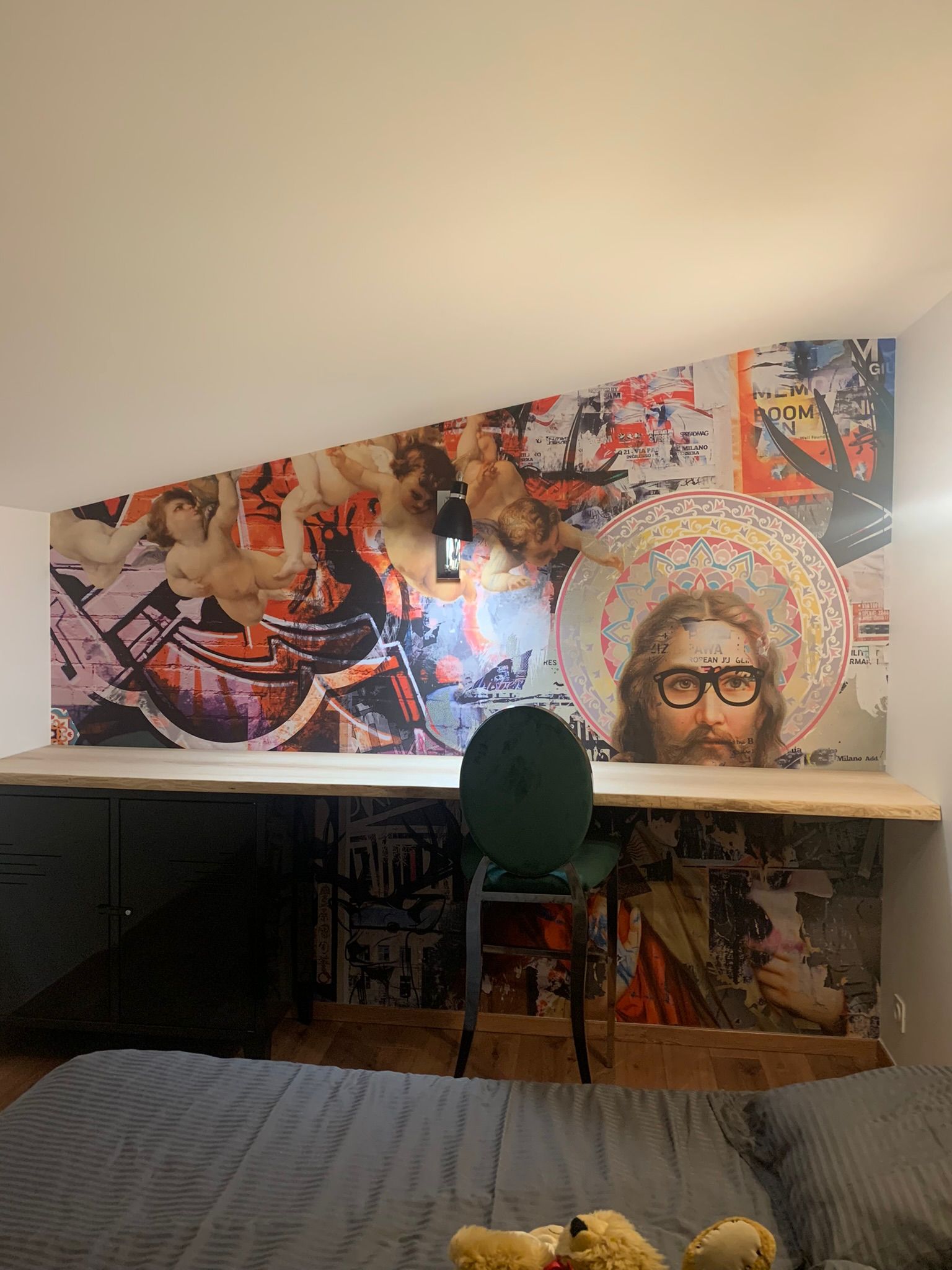 Mur de chambre orné d'une fresque représentant des personnages de style Renaissance et John Lennon portant des lunettes, au-dessus d'un bureau et d'une chaise en bois.