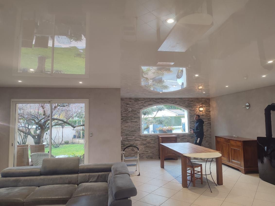 Salon avec plafond réfléchissant, canapé, table en bois et personne près d'une fenêtre.