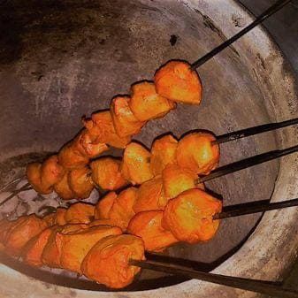 Brochetas de carne marinada en naranja asándose sobre brasas en un horno tandoor de barro.