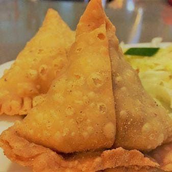 Tres samosas doradas en un plato, con repollo rallado al fondo.