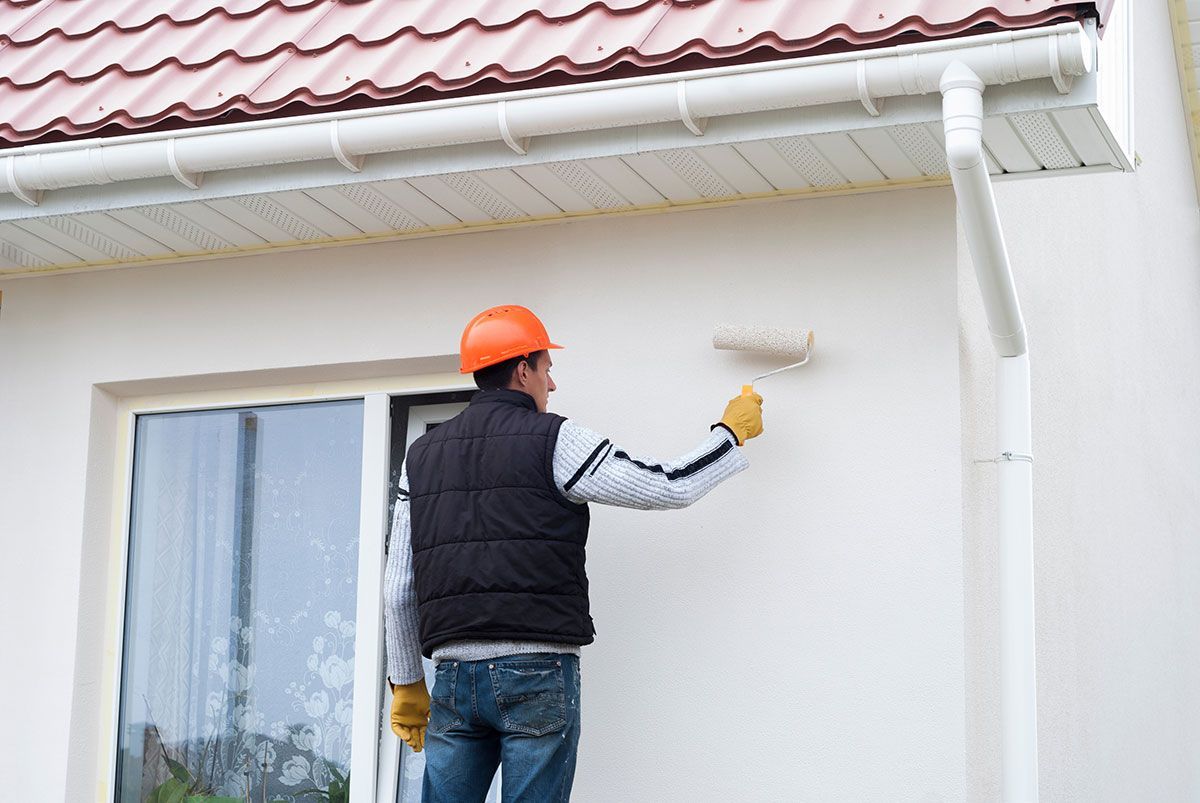 Homme avec un casque orange qui peint le mur extérieur d'une maison