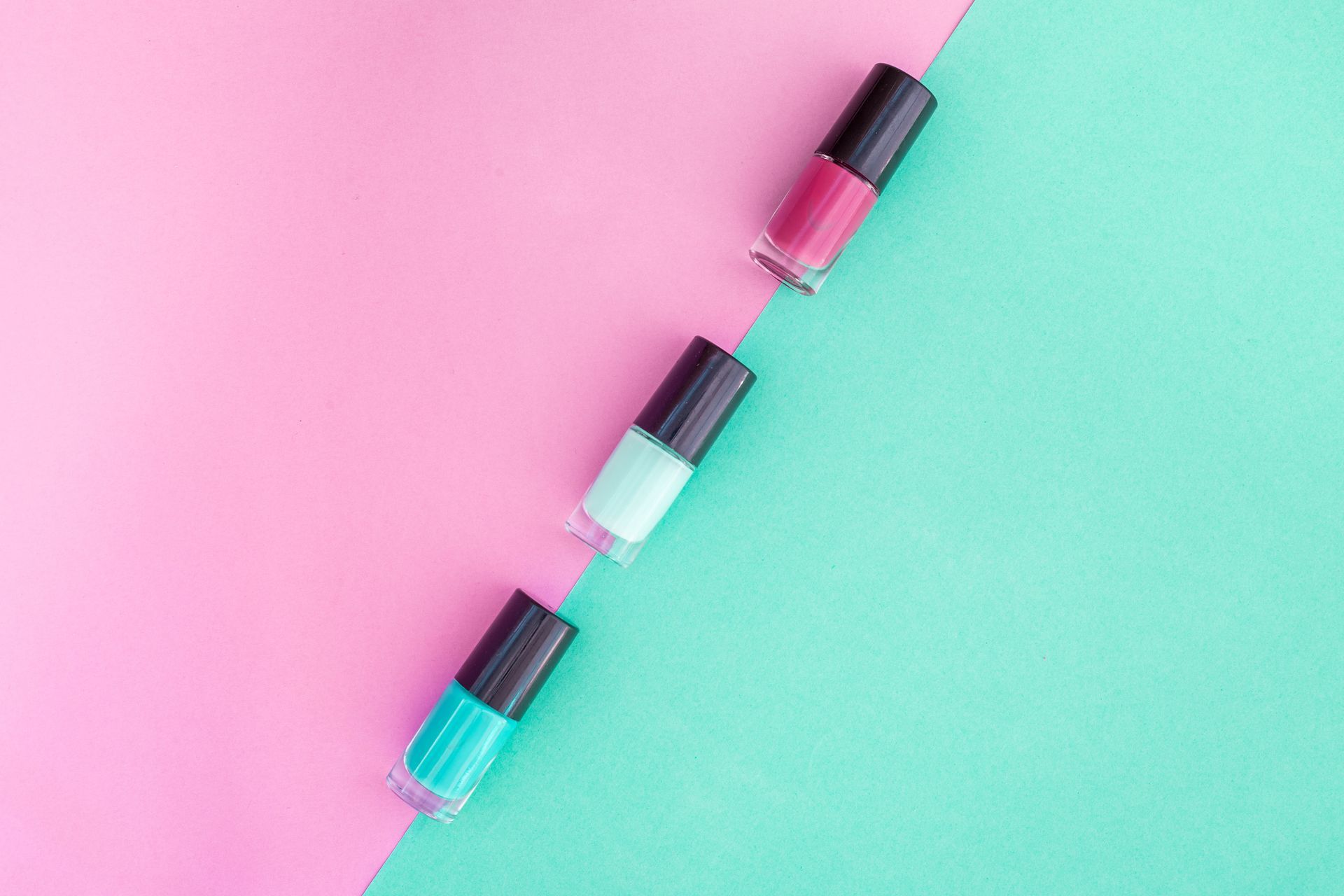Tres frascos de esmalte de uñas: verde azulado, menta y magenta sobre fondo diagonal rosa y verde.
