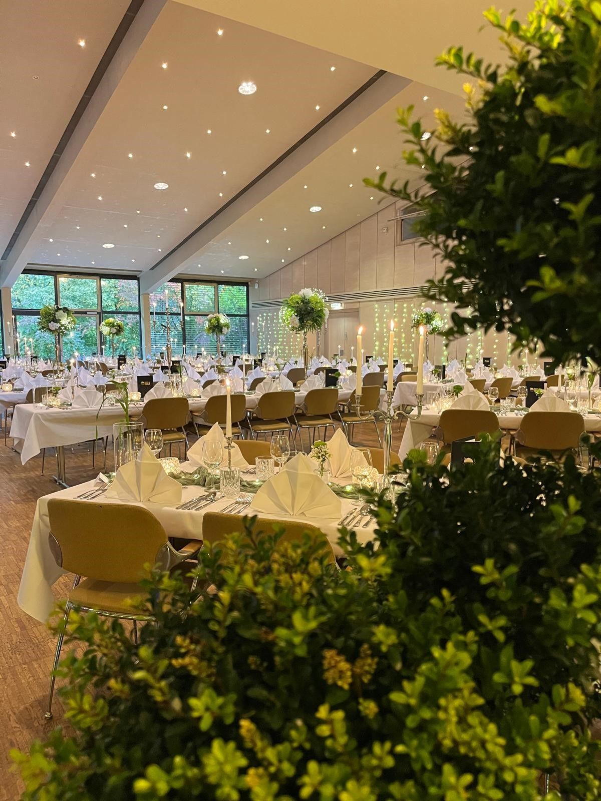 Empfangssaal für einen besonderen Anlass, Tische mit weißer Tischwäsche, Stühlen und Tafelaufsätzen.