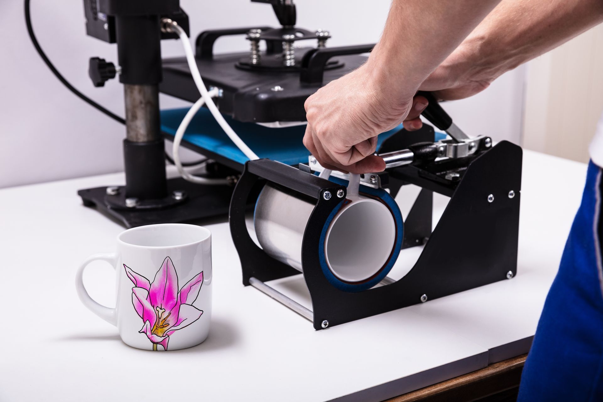 persona elaborando imágenes personalizadas en tazas. Taza blanca con flor rosa apoyada en la mesa.
