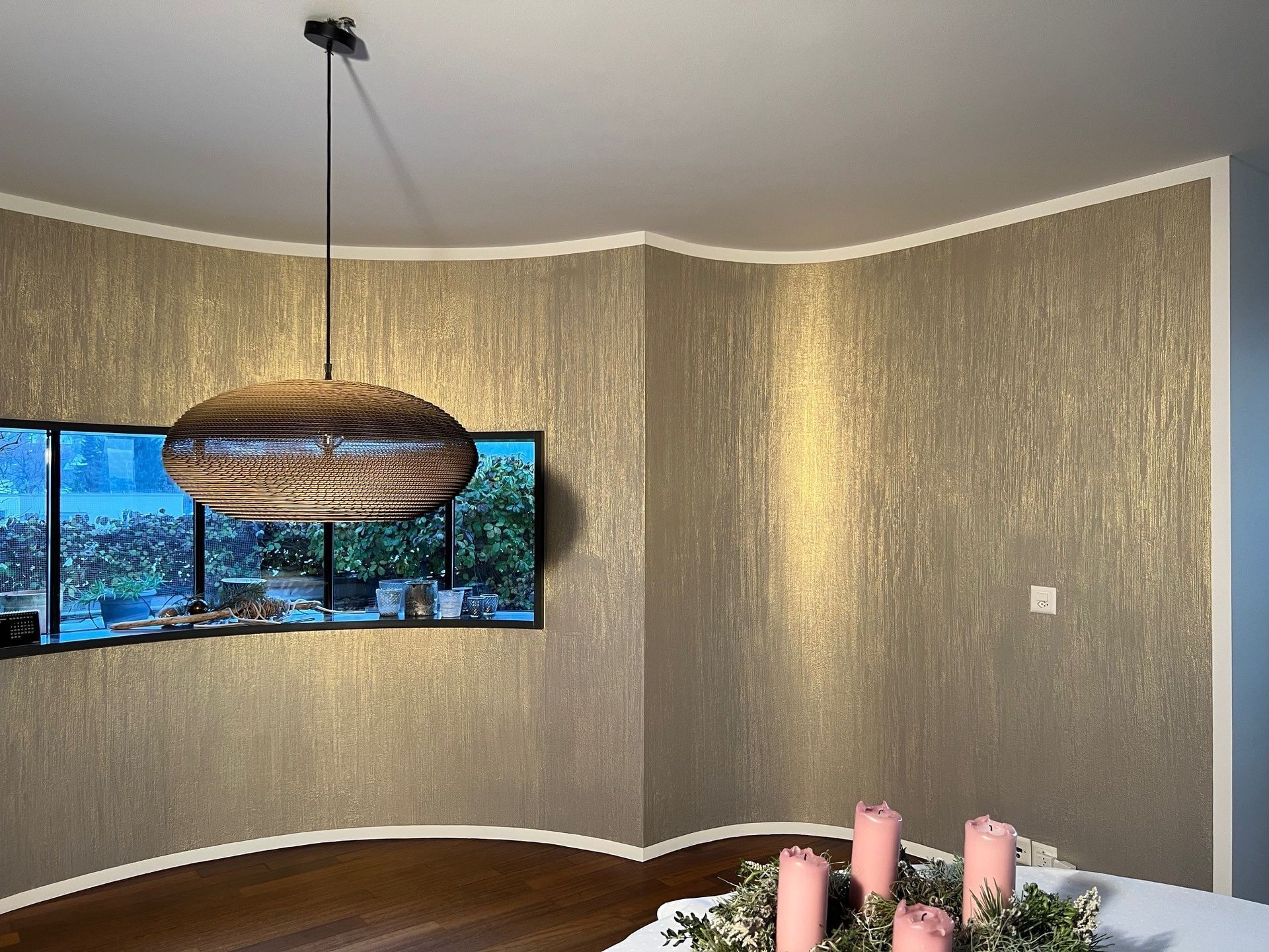 Eine mit Staub bedeckte Hand hält einen Pinsel und trägt einen weissen Anstrich auf eine raue, strukturierte Wand auf.