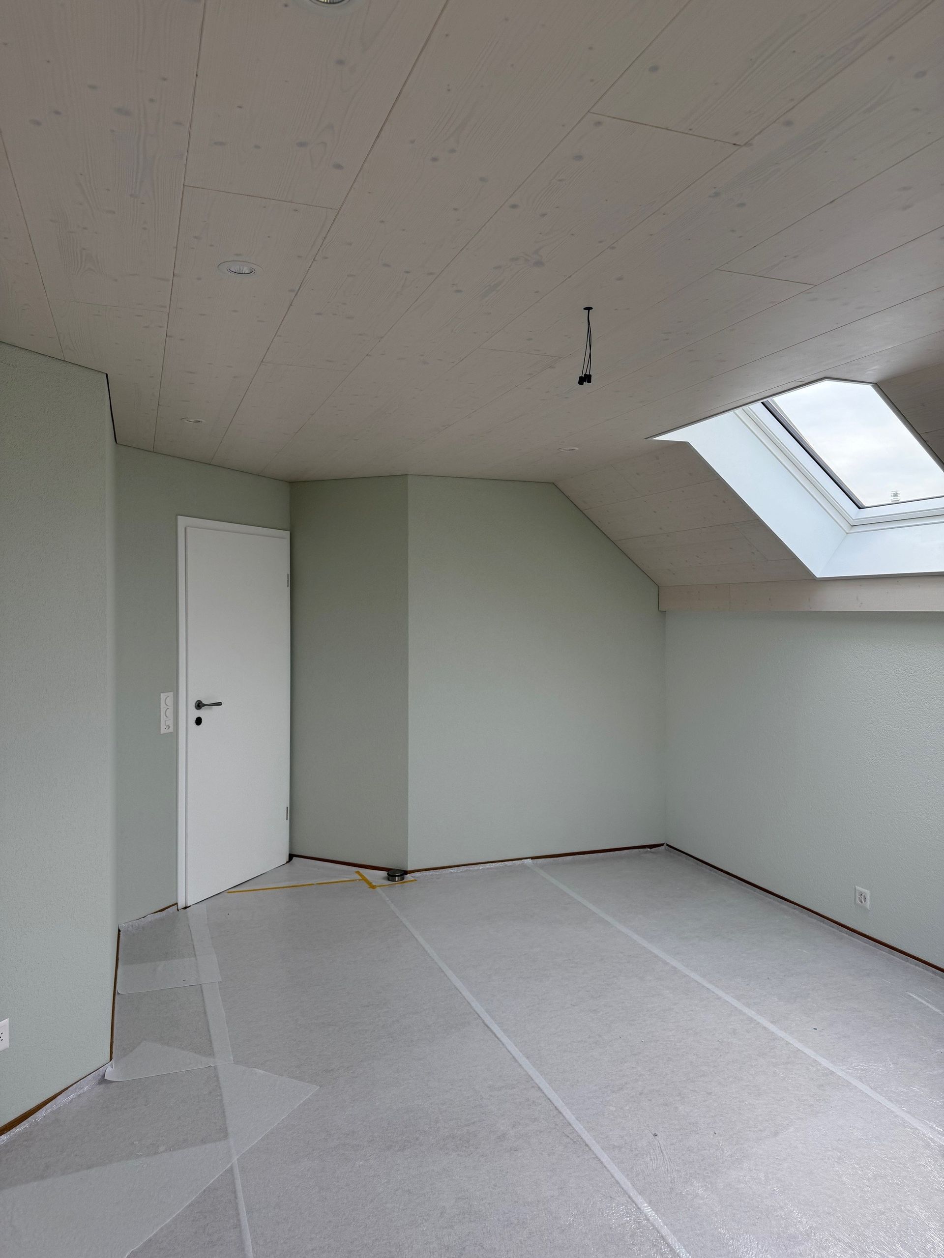 Eine Person in Arbeitshandschuhen trägt mit einer Spritzpistole eine rötlich-braune Holzbeize auf mehrere Holzplanken auf.