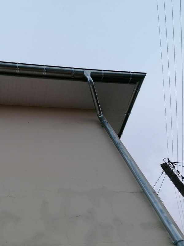Angle extérieur d'un bâtiment clair avec une gouttière métallique et des lignes électriques aériennes