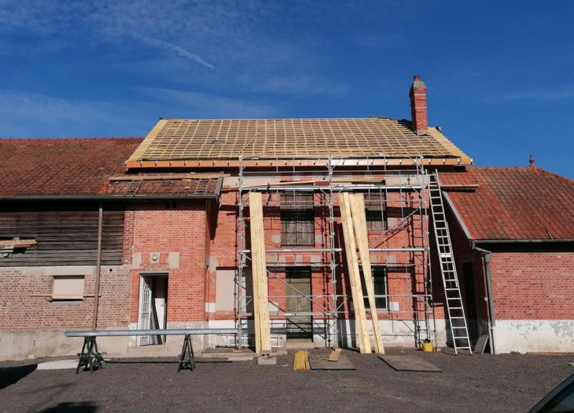 Échafaudages sur un bâtiment en briques au toit de tuiles rouges sous un ciel bleu