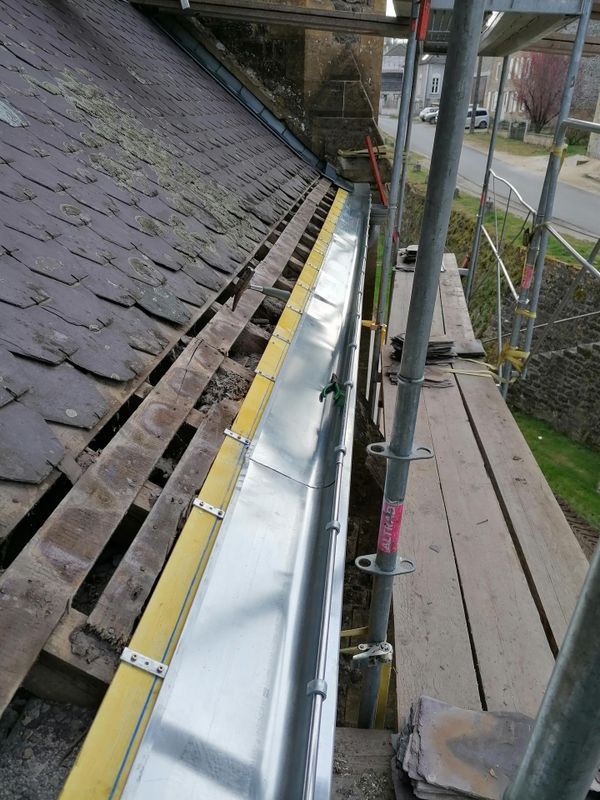 Réparation de la toiture avec échafaudage et pose d'une nouvelle gouttière métallique le long du bord du toit en ardoise.