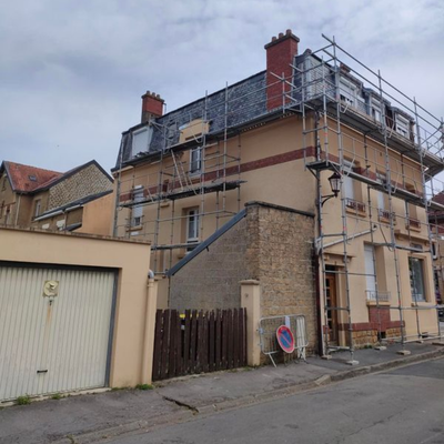 Maison à deux étages en rénovation, avec échafaudages à côté d'un garage dans une rue calme.