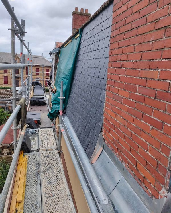 Échafaudage à côté d'un mur de briques et d'un toit en ardoise en réparation.