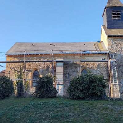 L'extérieur d'une église en pierre, avec ses murs couverts de lierre et son clocher.