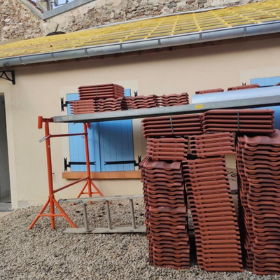 Des piles de tuiles en terre cuite sont entreposées sur des étagères devant un bâtiment à la porte bleue.