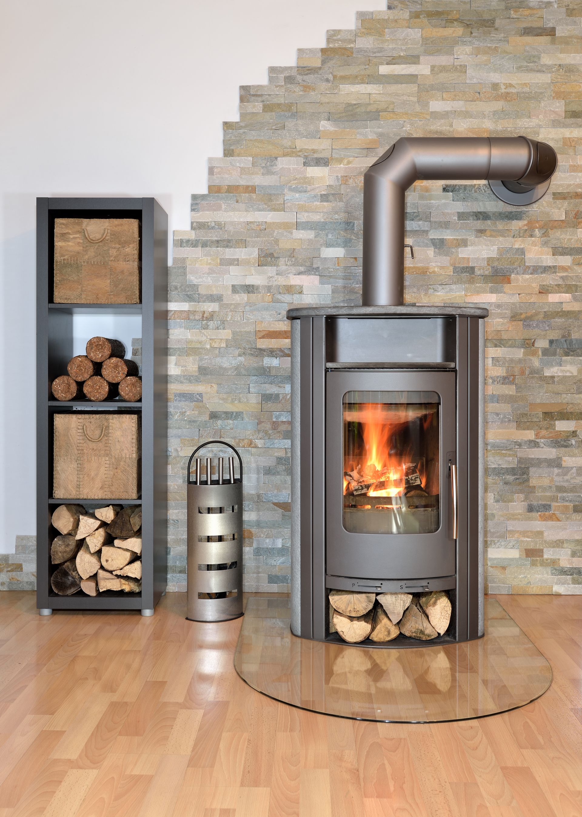 Poêle à bois moderne allumé dans un salon, à côté d'une pile de bois de chauffage et d'un conduit de cheminée en acier inoxydable.