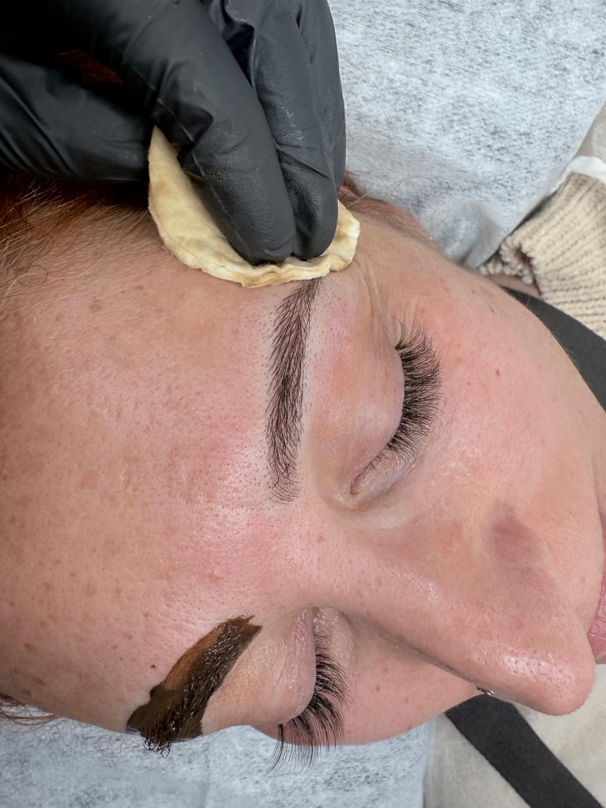 Una mujer se pinta las cejas con una persona que lleva guantes negros.