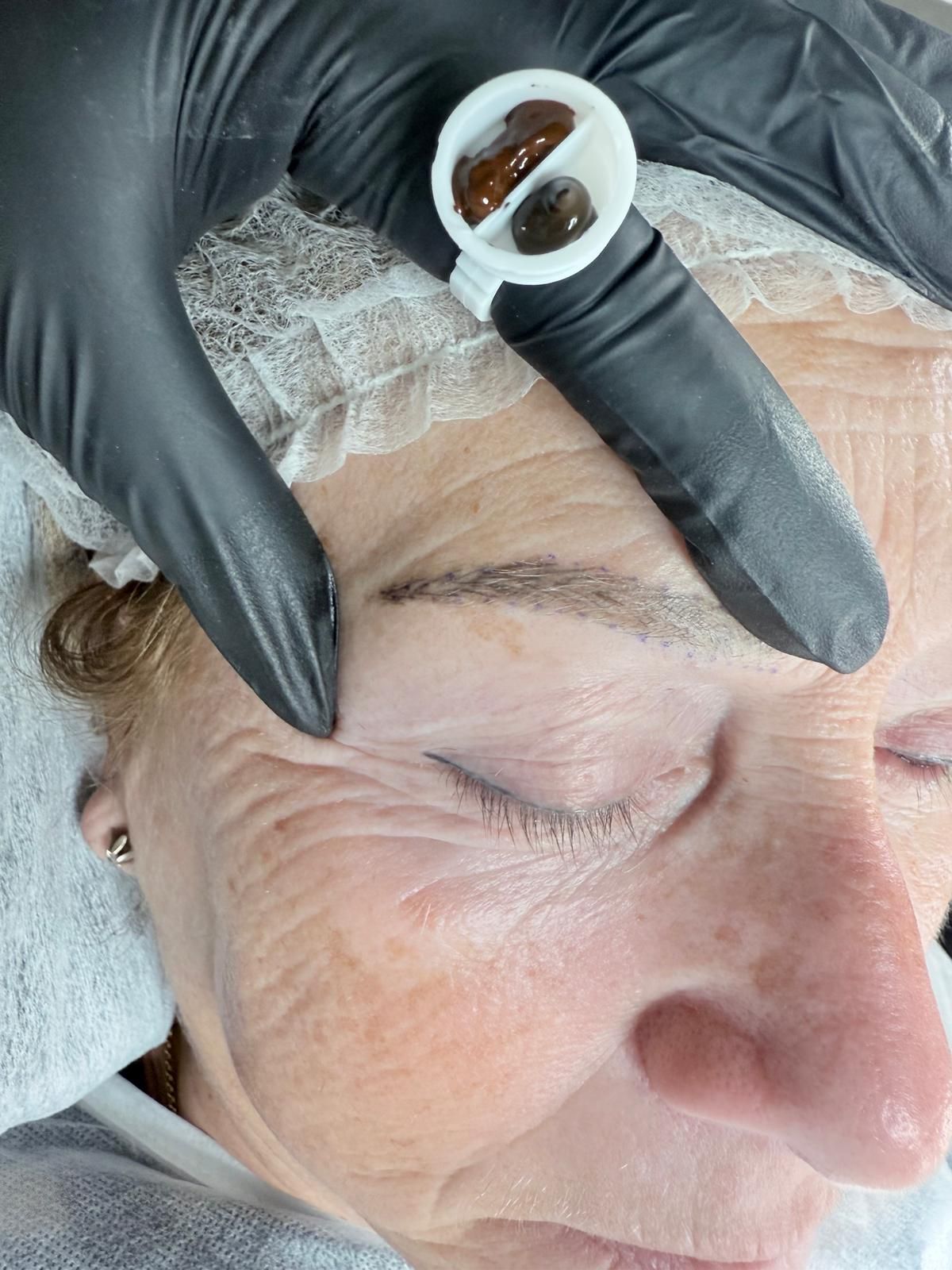 Una mujer se pinta las cejas con una persona que lleva guantes negros.