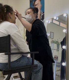 Una mujer que lleva una máscara está aplicando maquillaje a otra mujer.