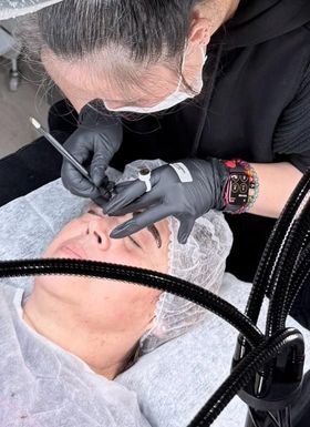 Una mujer que lleva una máscara y guantes negros está aplicando maquillaje en las cejas de una mujer.