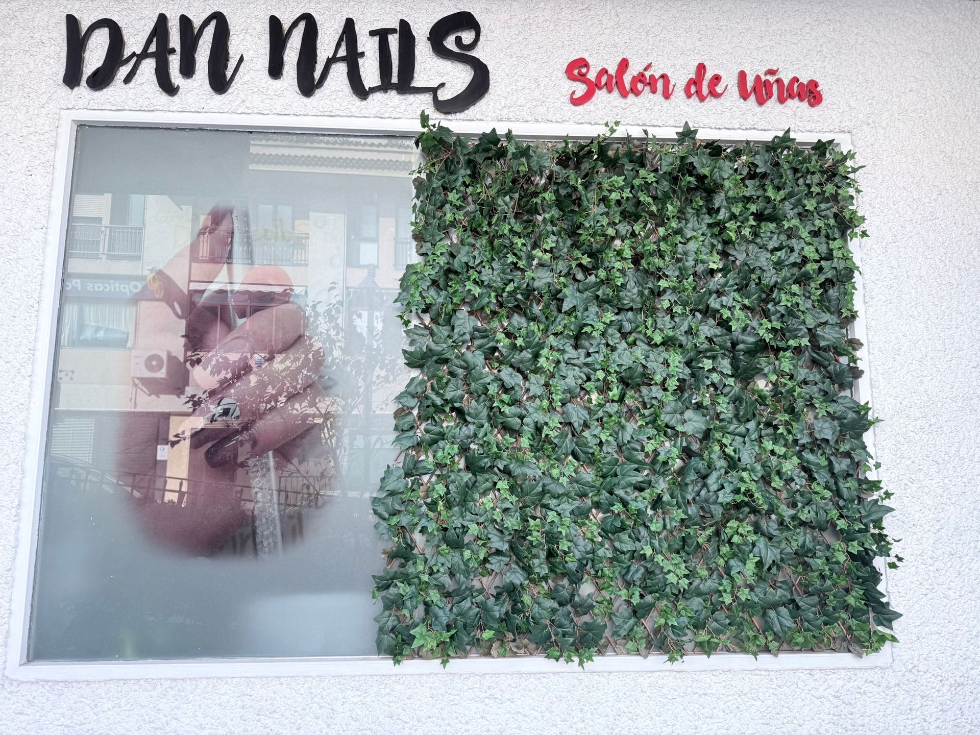 Una persona se toma una fotografía de la mano en la ventana de un salón de uñas.