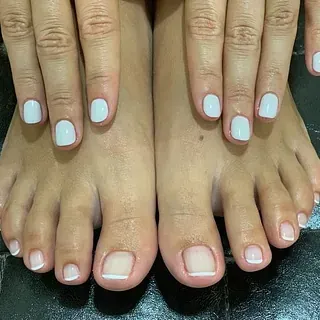 Un primer plano de los pies y las manos de una mujer con uñas blancas.
