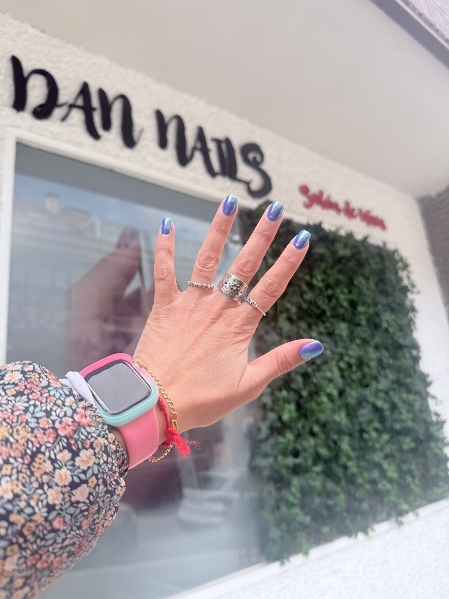 La mano de una mujer con uñas azules y un anillo está parada frente a un edificio.