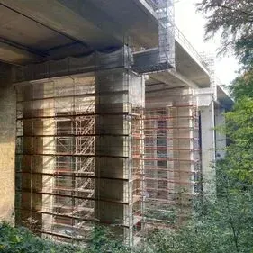 Eine im Bau befindliche Brücke mit Gerüsten und Bäumen im Hintergrund.