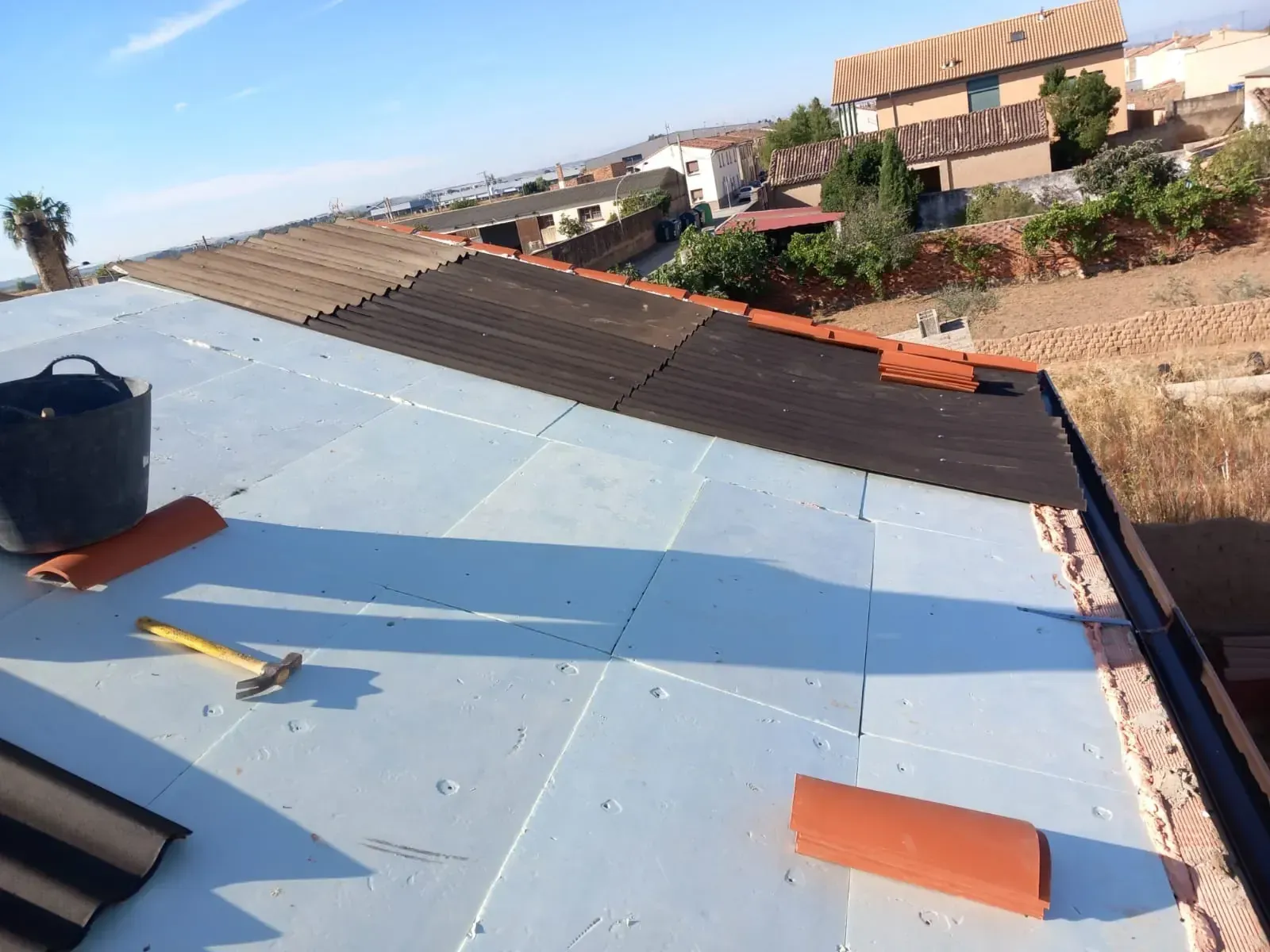 Techo parcialmente cubierto con aislante y tejas, con herramientas y balde.