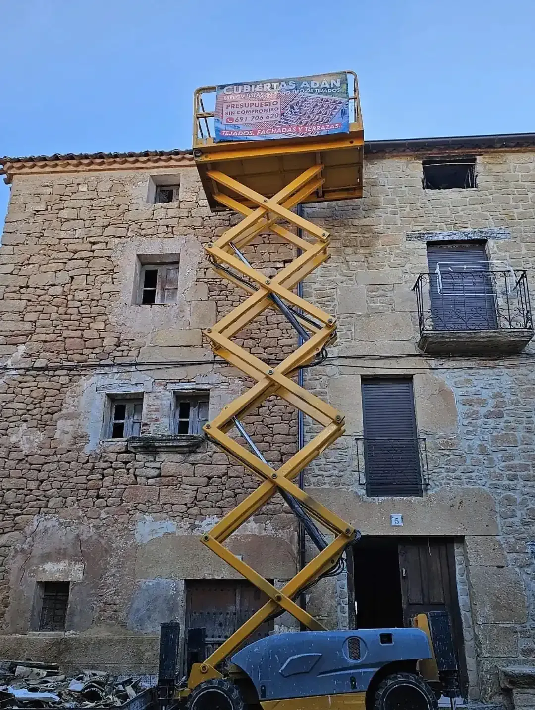 Elevador de tijera amarillo extendido hasta antiguo edificio de piedra.