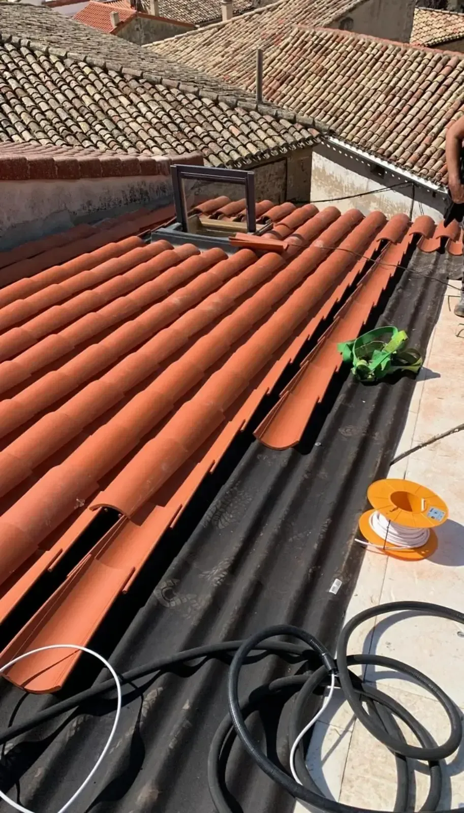 Azotea con tejas naranjas y equipamiento: rollos de alambre, tela verde y cable negro.