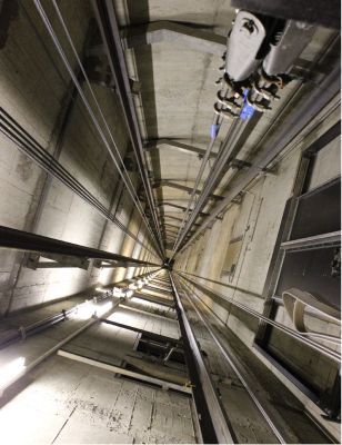 Vista hacia arriba de un pozo industrial vertical con cables de ascensor y maquinaria en la parte superior.