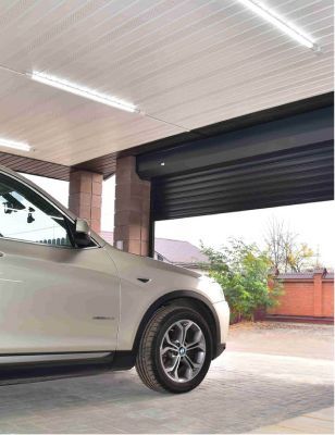 SUV blanco estacionado bajo una entrada techada con una puerta de garaje negra cerrada detrás.