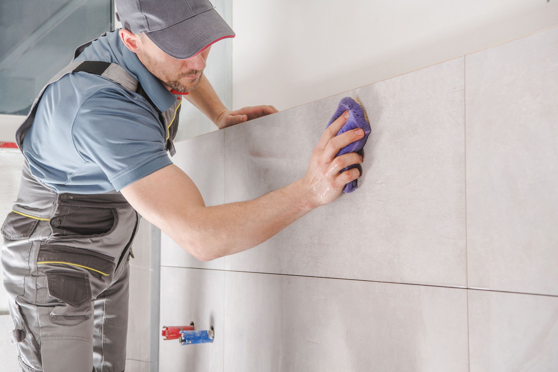 Un ouvrier nettoie de grands carreaux muraux avec une éponge violette dans une salle de bains lumineuse