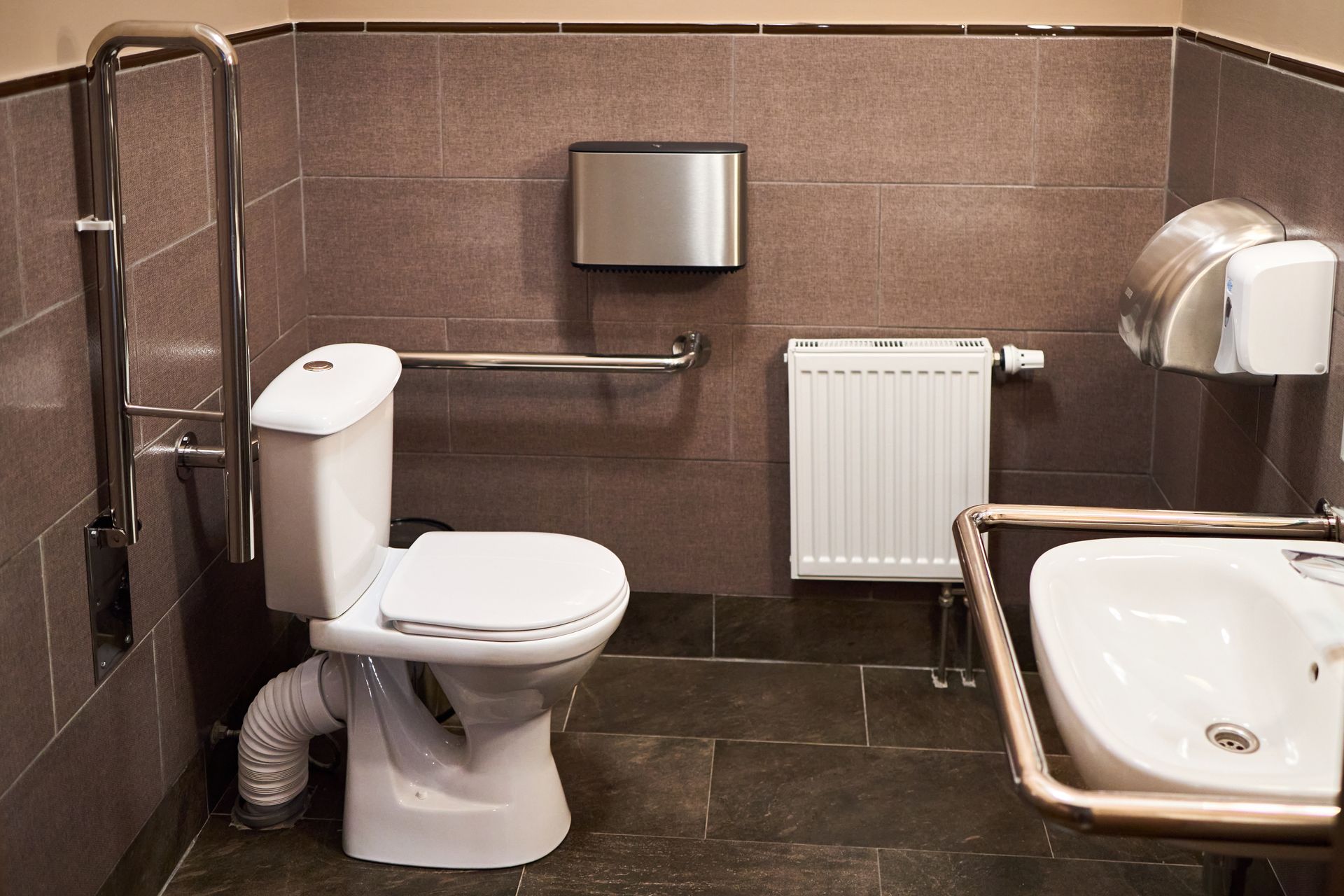 Salle de bains accessible avec toilettes, lavabo, barres d’appui et distributeur de papier mural.