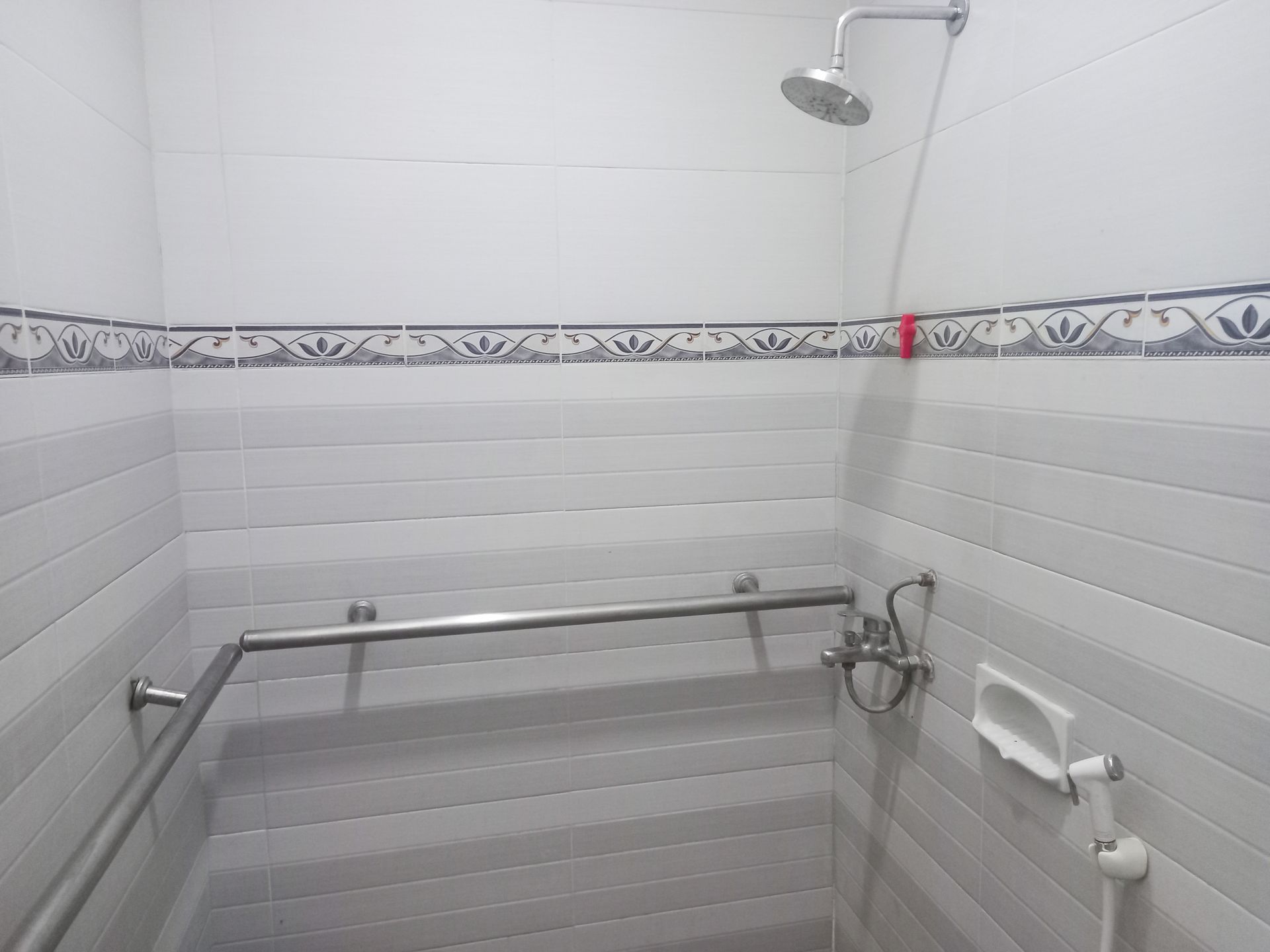 Douche de salle de bains accessible avec barres d’appui, siège rabattable et murs carrelés en blanc.