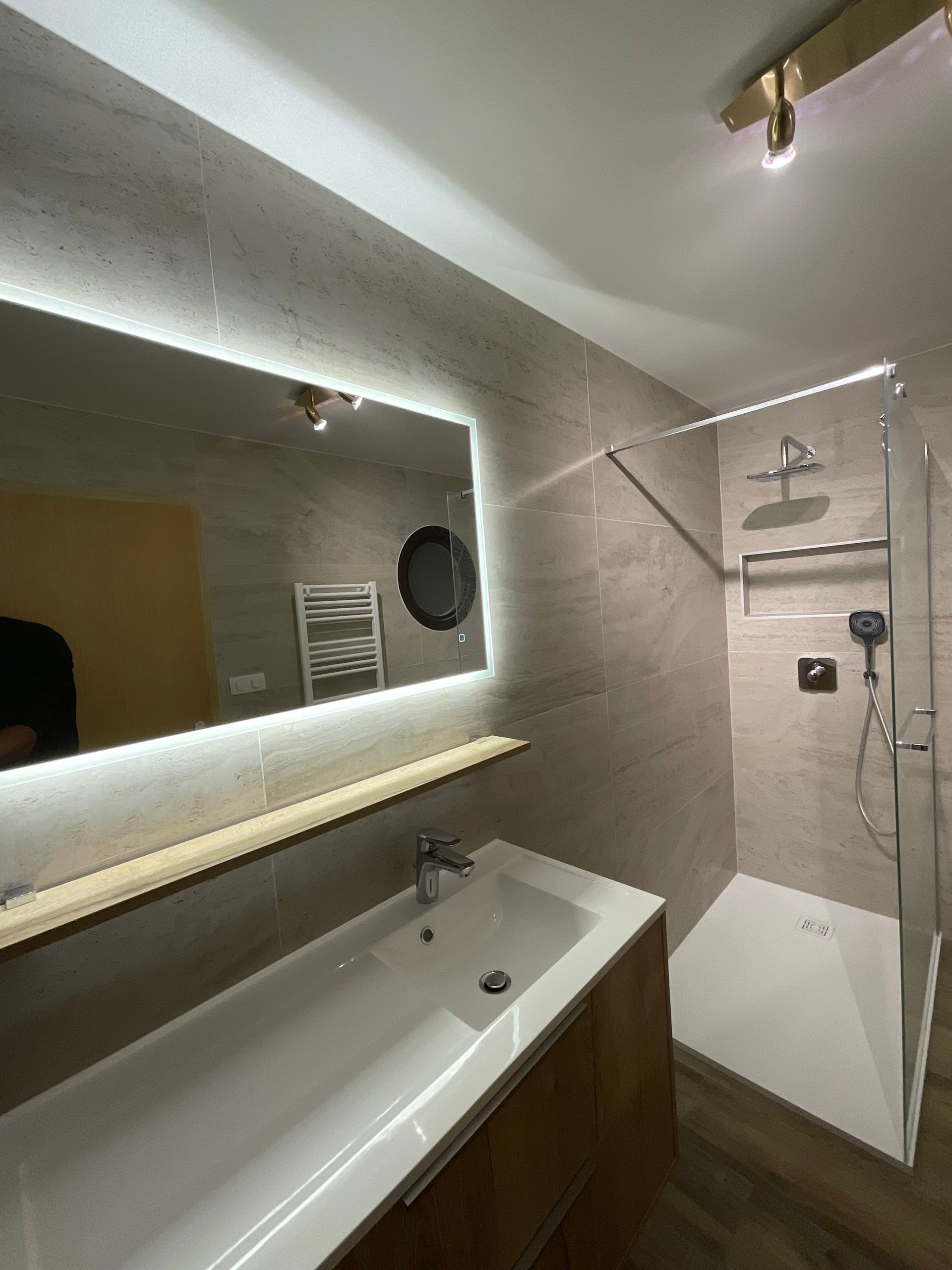 Salle de bains moderne avec un grand miroir, un meuble vasque, une douche et un éclairage tamisé
