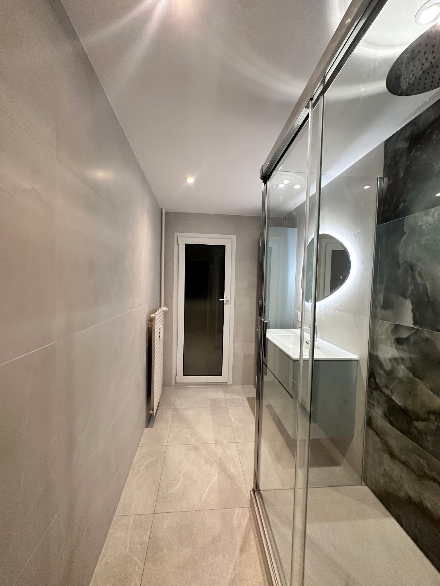 Couloir étroit avec des portes de placard à miroir, des murs gris et une porte au fond.