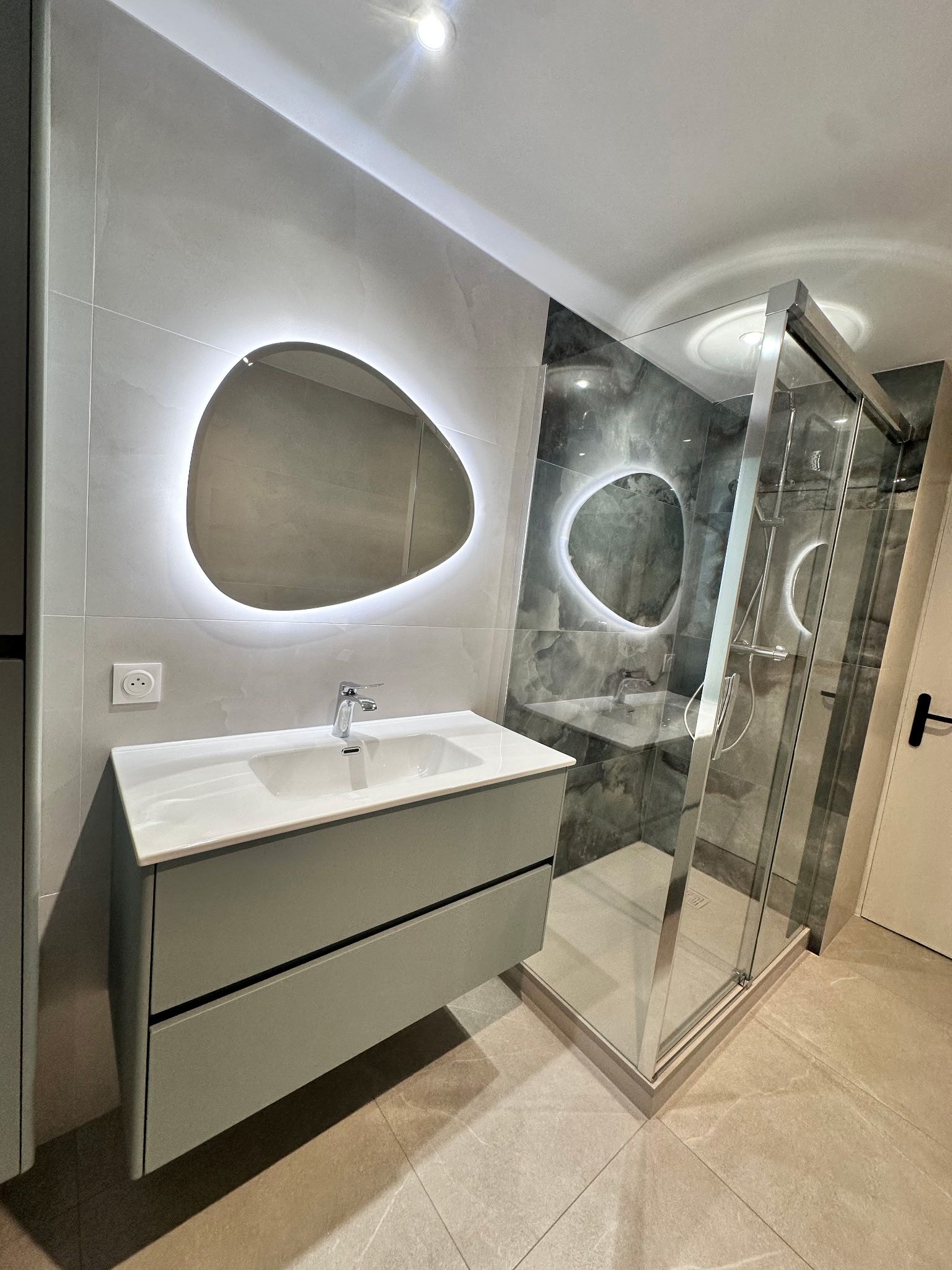 Salle de bains moderne avec lavabo suspendu, miroir ovale et paroi de douche en verre.