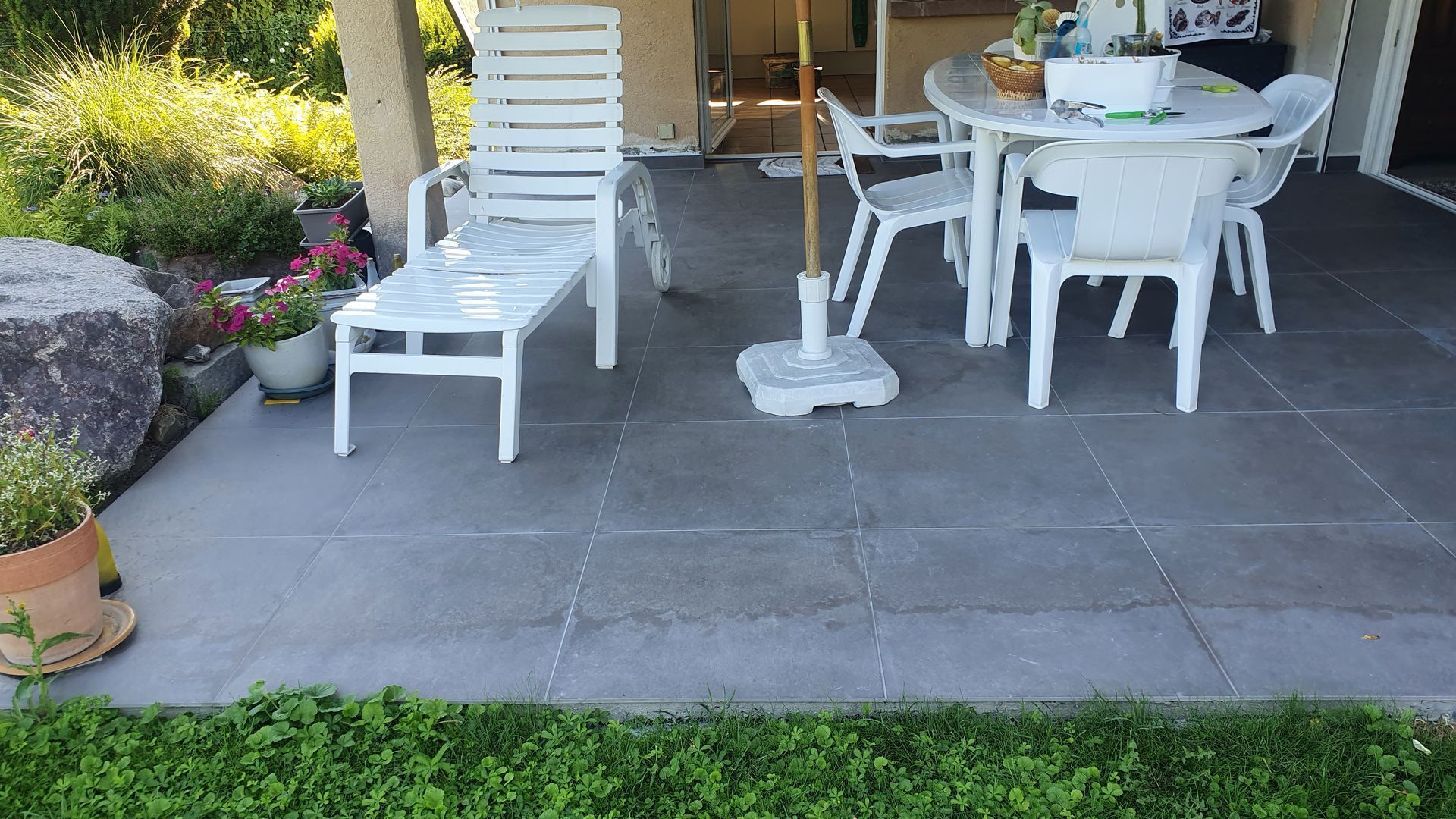 Ensemble de chaise et de table de patio blanc sur une terrasse carrelée, près d’une pelouse et d’un jardin verdoyants.