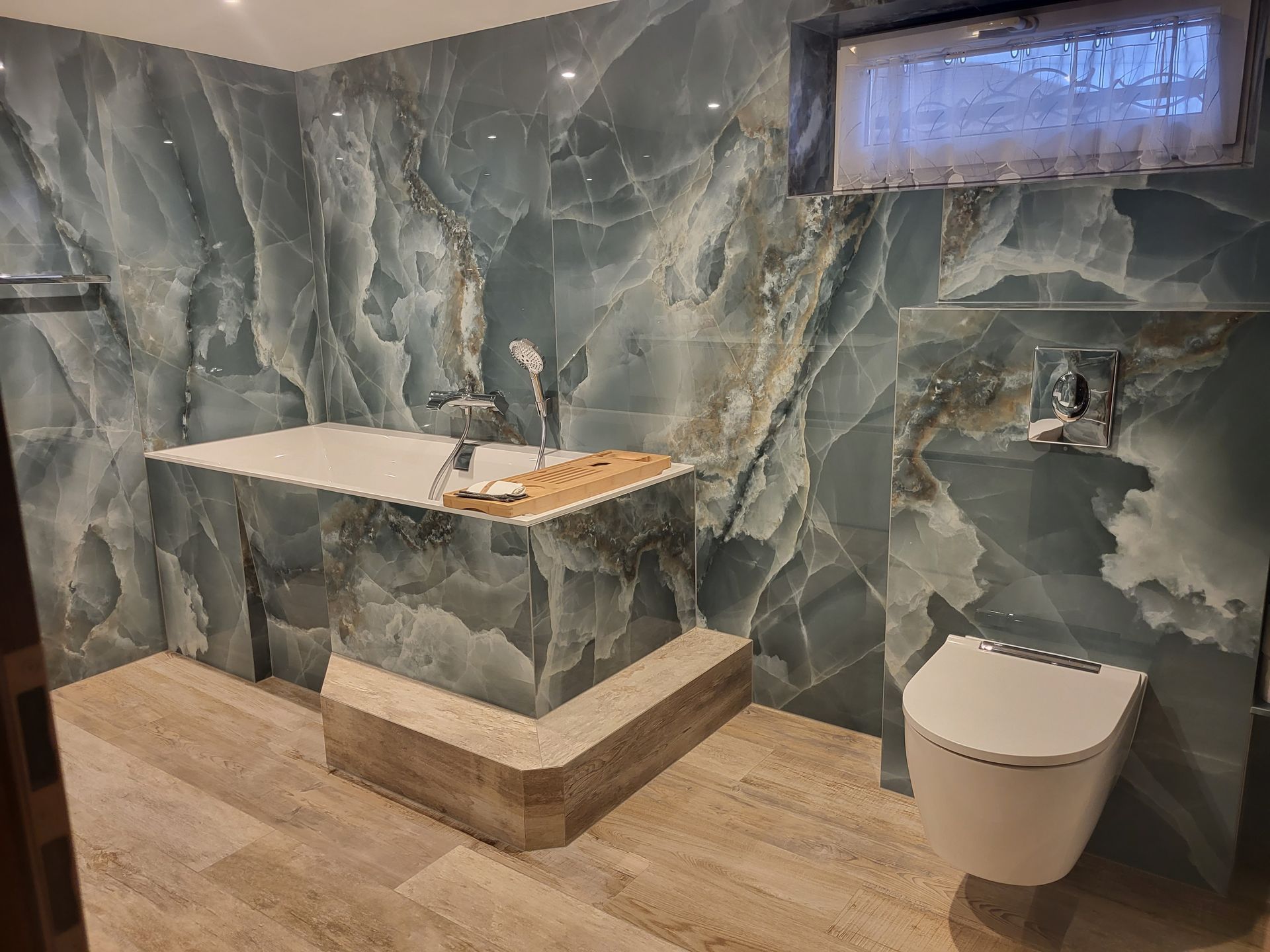 Salle de bains moderne avec murs en marbre bleu, lavabo suspendu, toilettes et sol en carrelage beige.