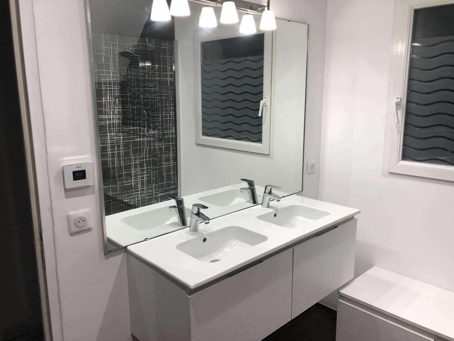 Salle de bains moderne avec double vasque, miroir mural et douche carrelée.