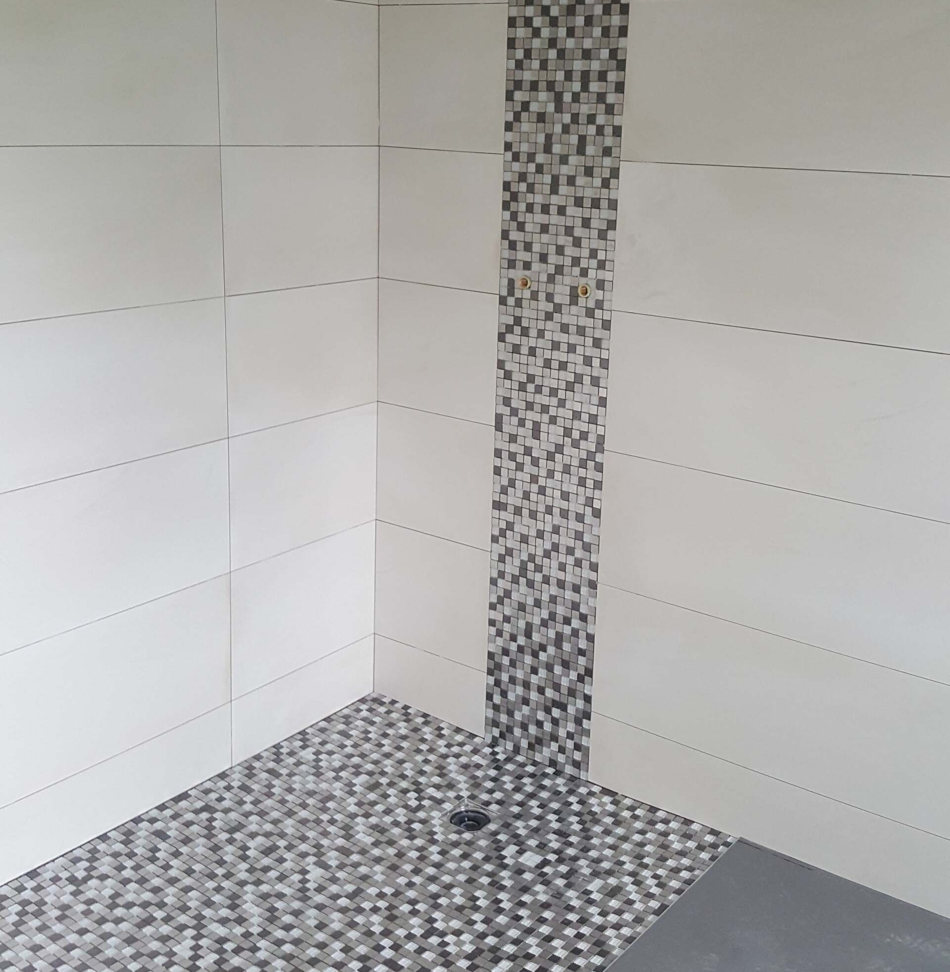 Petit coin douche dans une petite salle de bains, avec des carreaux blancs aux murs, un sol en mosaïque grise et une bande décorative
