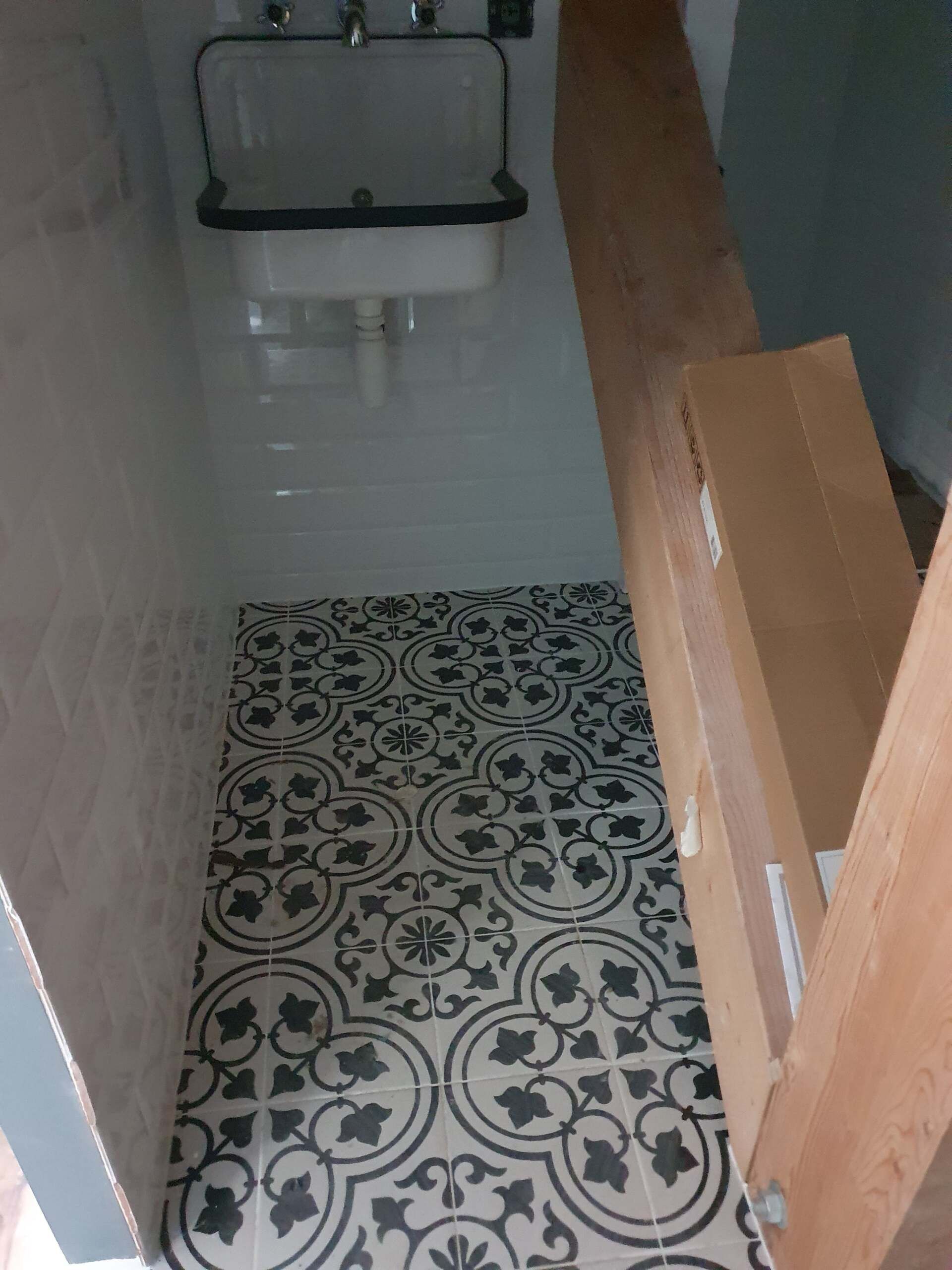 Couloir étroit carrelé au sol à motifs, menant à un lavabo mural et à un miroir.