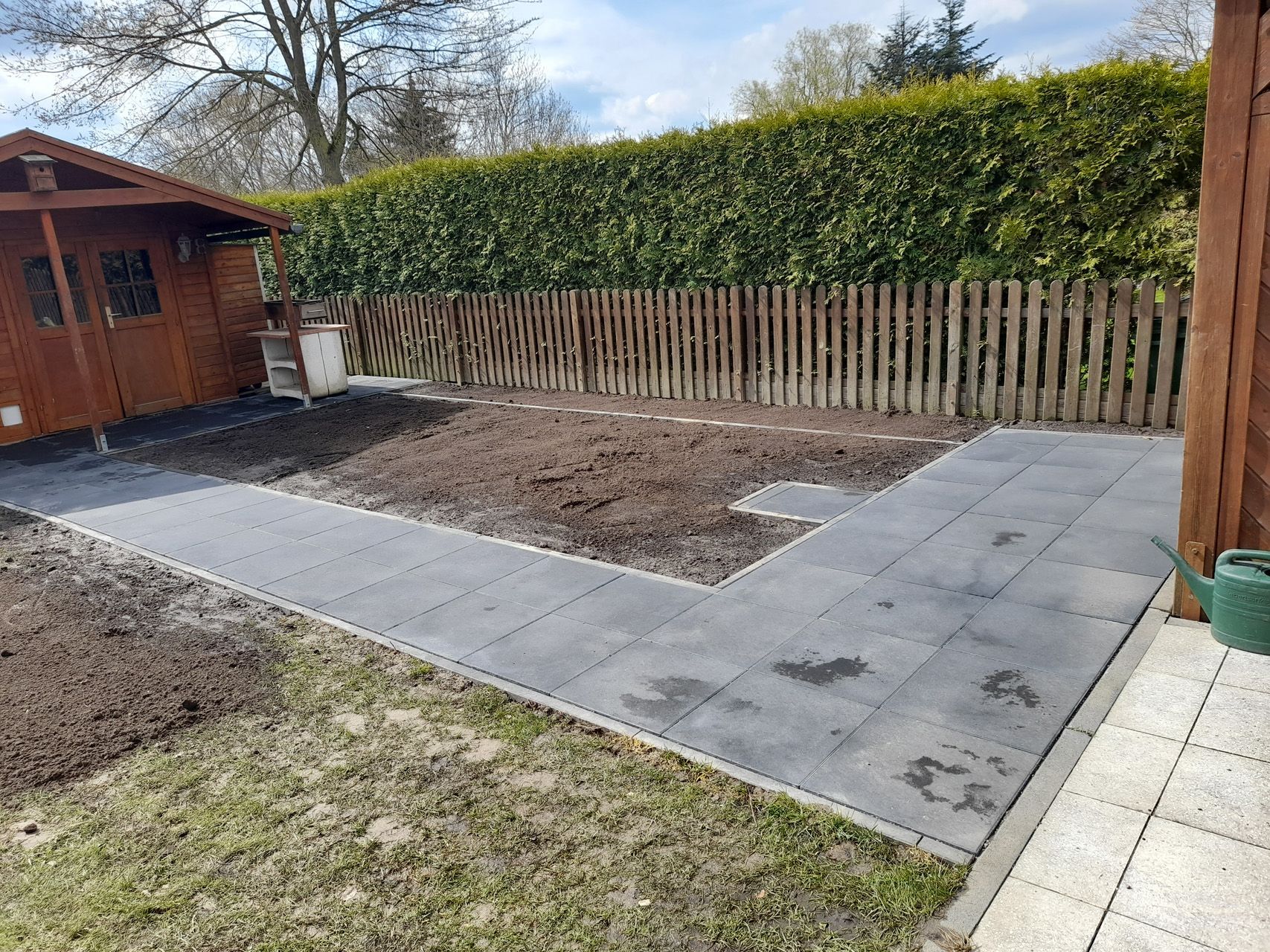 Ein Holzschuppen steht mitten in einem Garten neben einem Zaun.