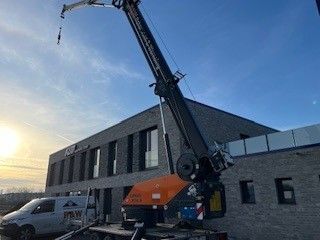 Ein Kranarm ist in der Nähe eines Backsteingebäudes ausgefahren. Ein Lieferwagen ist daneben geparkt.