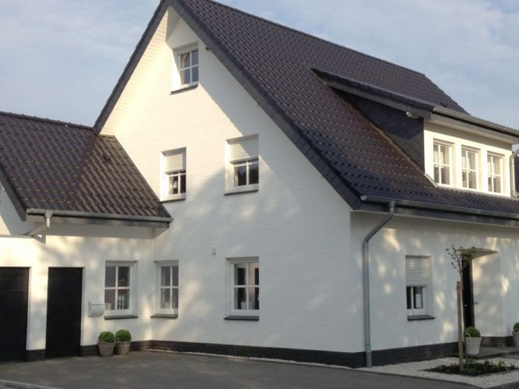 Weißes zweistöckiges Haus mit schwarzem Dach und Zierleisten. Fenster und Haustür sind sichtbar.