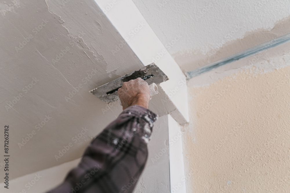 Une personne lisse une cloison sèche à la truelle dans un angle de plafond.